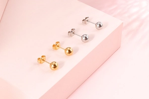Minimalist gold and silver spherical stud earrings displayed on pink geometric shapes
