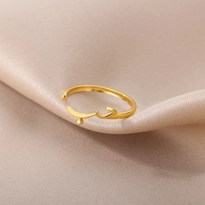 Close-up of gold Arabic letter open ring displayed on soft beige satin fabric