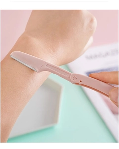 Pink folding eyebrow razor with safety guards trimming facial hair on skin macro view