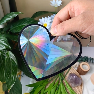 Hand holding a heart-shaped suncatcher showing vibrant rainbow holographic light effects