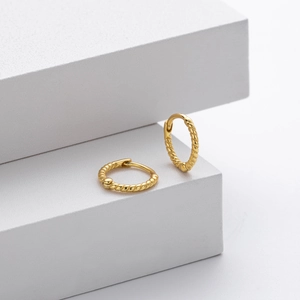 Macro detail of golden twisted hoop earrings on minimalist white geometric pedestals