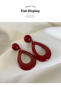 Detail view of red resin teardrop earrings with smooth glossy finish on white fabric