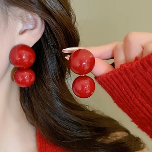 Detail view of red glossy double sphere earrings paired with a red knitted sweater