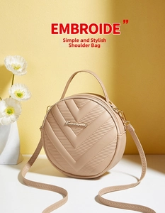 Detail view of round beige V-pattern handbag with top handle and metallic logo plate