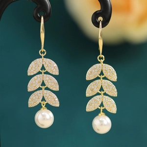 Macro shot of elegant golden leaf earrings with shimmering zircon and white round pearls