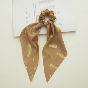 Detail of a brown silk hair scrunchie with gold feather patterns on a magazine