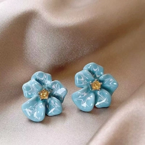 Détail de boucles d'oreilles fleur bleue avec pierre jaune sur soie champagne