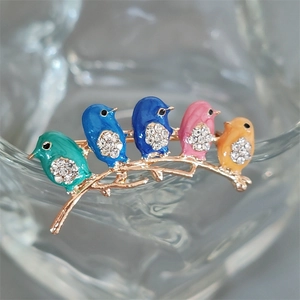 Close-up of colorful enamel bird brooch with sparkling rhinestones on a golden branch
