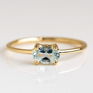 18k gold plated stainless steel ring with oval light blue birthstone on white surface