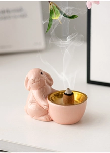 Detailed view of a pink ceramic rabbit incense burner with golden bowl and smoke