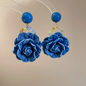 Détail de boucles d'oreilles rose en denim avec perles bleues et texture de tissu