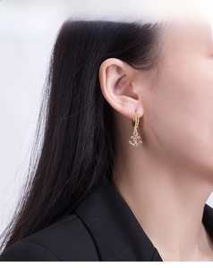 Detail showing a gold anchor earring with colorful crystals on a female model profile