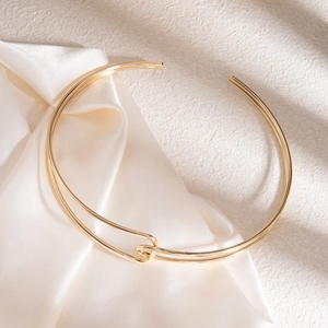 Détail d'un collier à nœud en spirale doré posé sur un tissu en soie beige