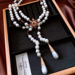 Detailed close-up of retro pearl necklace with amber gemstone and teardrop pendants