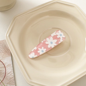 Detailed view of a pink acrylic hair clip with white daisy patterns on a beige tray