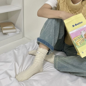 Cozy cream ruffle trim slouch socks with vertical stripes shown in a lifestyle bedroom setting