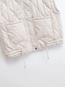 Detail view of beige quilted vest showing front pockets and adjustable drawstring hem