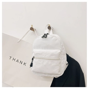 Minimalist white nylon mini backpack hanging on wooden hook with stylish outfit accents