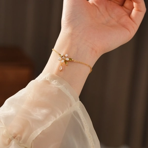 Dettaglio di un bracciale dorato con fiore in smalto bianco e cristalli brillanti