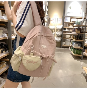 Pink nylon backpack detail showing side pockets and lucky heart charm accessory