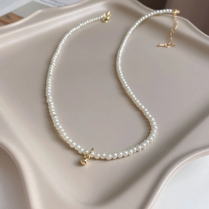 Élégant collier de perles blanches avec perle dorée centrale sur une assiette en céramique