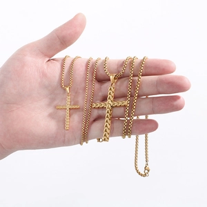Vue macro de deux pendentifs croix de blé en acier doré tenus en main pour la taille