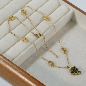 Golden hollow smiley face pendant necklace with green stones on a white jewelry display