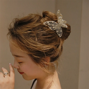 Detailed close-up of golden butterfly hair claw clip with faux pearl embellishments