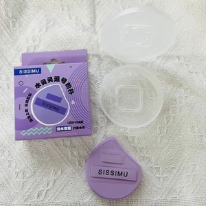 Close-up of a purple comma-shaped makeup sponge with storage box and paper packaging