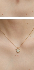 Macro detail of gold heart pendant with white shell inlay on beaded chain necklace