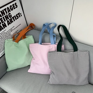 Detailed shot of striped canvas tote bags in green pink and black on a soft grey sofa