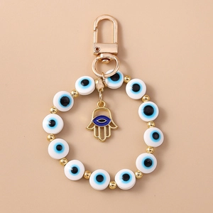 Detail of Hamsa hand and blue evil eye beads on golden keychain for bag decor