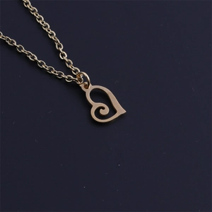 Detailed view of a golden stainless steel heart pendant necklace on a dark matte surface