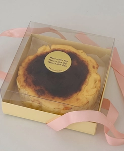 Detail of Basque cheesecake in a clear square box with a decorative pink ribbon tie