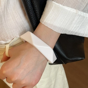 Close-up of white resin geometric bangle with polished triangular cross-section on wrist