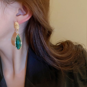 Close-up of vintage emerald glass teardrop earrings on model with golden metal setting