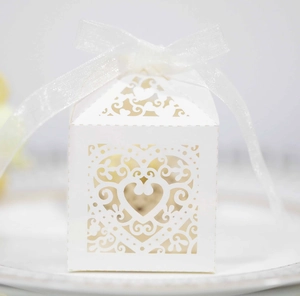 Close-up of laser-cut white wedding favor box with heart pattern and white silk bow