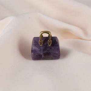 Detailed view of mini purple amethyst handbag pendant with gold handle on beige fabric
