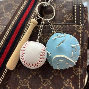 Detailed view of mini wooden baseball bat and glove keychain hanging on a stylish bag