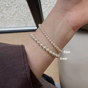 Detail shot of 4mm and 6mm white pearl elastic bracelets on model wrist for sizing comparison
