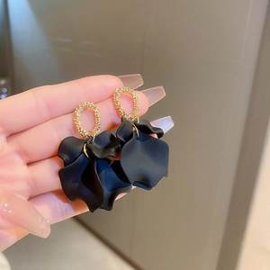 Close-up of black matte petal earrings with gold glitter rings held by hand