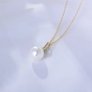 Close-up of a gold pearl necklace with zircon inlay on a soft white silk fabric