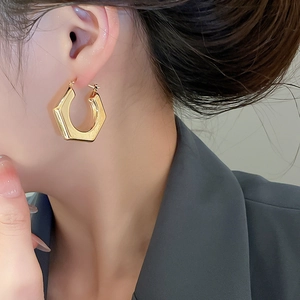 Detailed close-up of polished gold hexagonal hoop earrings worn with a formal suit