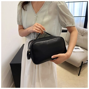 Close-up of black leather makeup bag with handle held by a model in a home setting