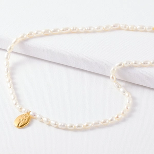 French vintage pearl necklace with golden rose relief coin pendant on white fabric