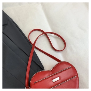 Detailed view of a red heart-shaped shoulder bag on a white fabric background