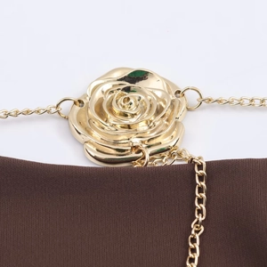 Makro-Detail einer goldenen Metallrose mit feiner Kette auf dunkelbraunem Stoff