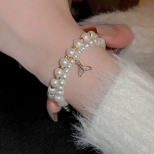 Double-layered pearl bracelet with a gold fishtail charm and shimmering zircon accents