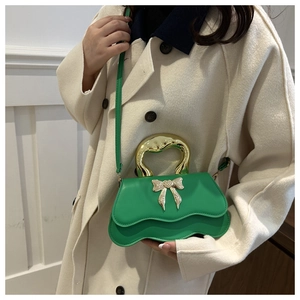 Detail of green handbag with wavy edge, metal handle and rhinestone bow buckle