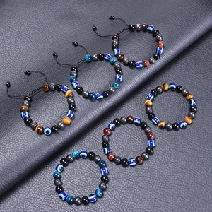 Dettaglio dei bracciali in pietre Occhio di Tigre e Evil Eye su sfondo di pelle nera